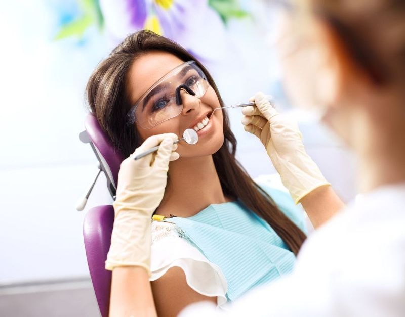 A woman is sitting in a dental chair while a dentist examines her teeth.