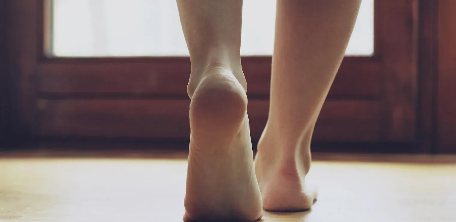 Bare feet walking across a wooden floor toward a bright window