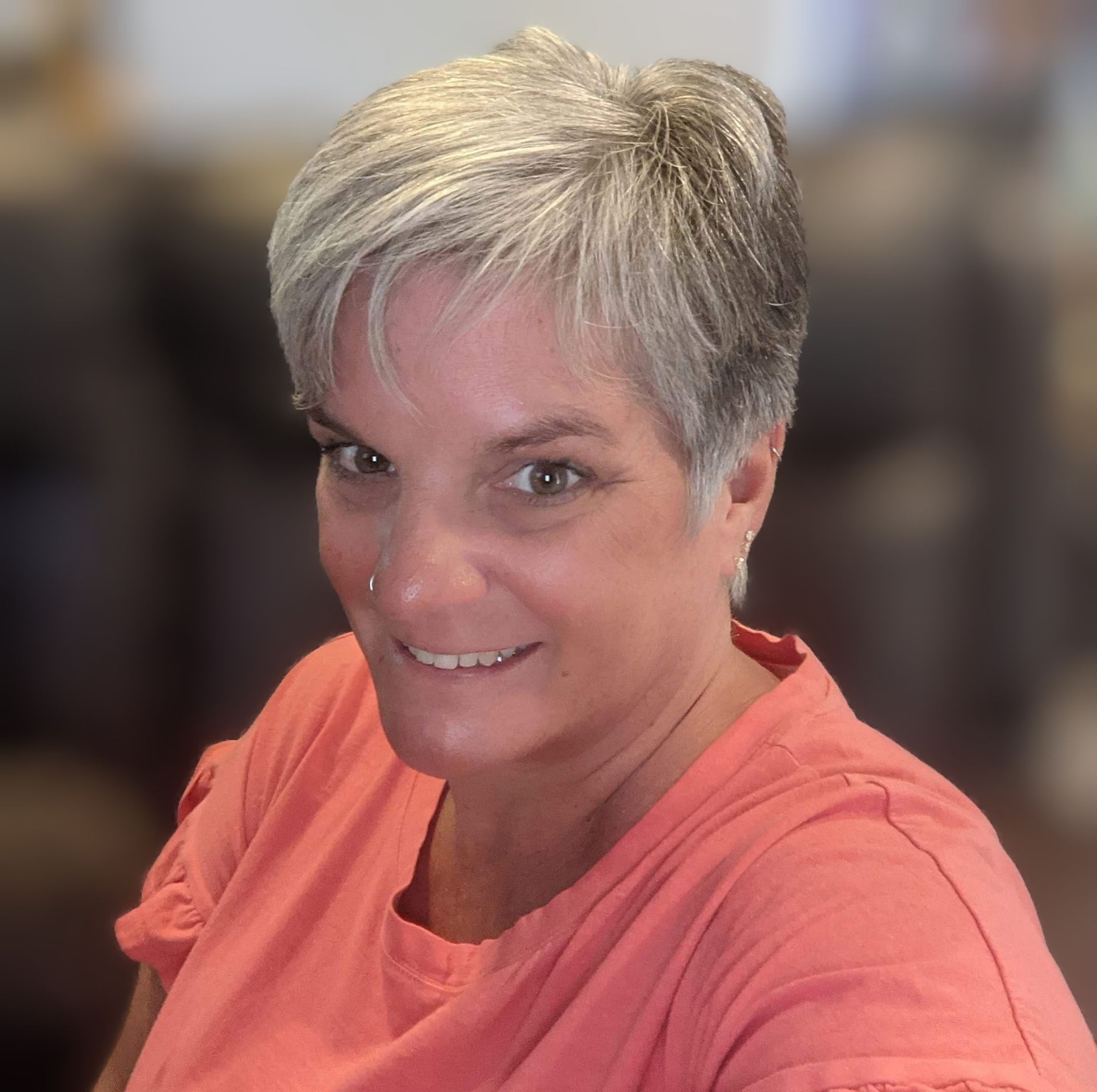 A woman is sitting at a desk with a laptop and a vase of flowers.