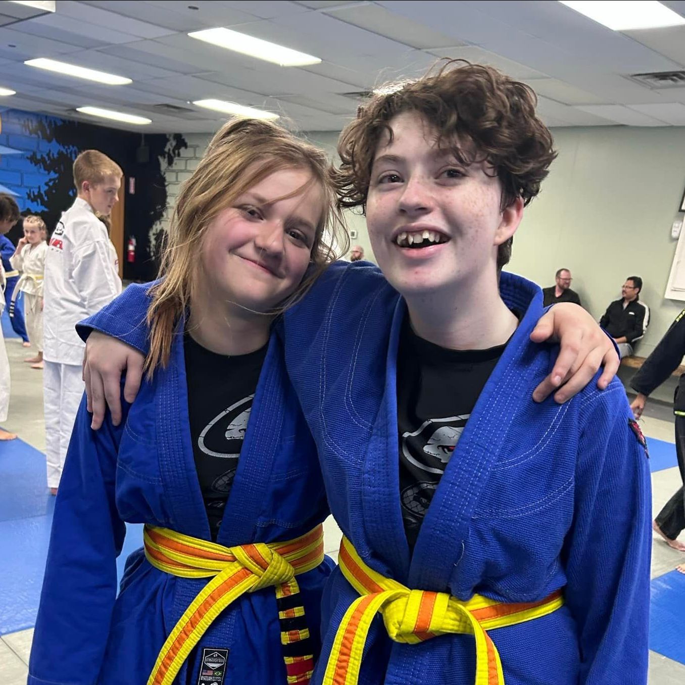 Two girls in blue kimonos with yellow belts are posing for a picture.