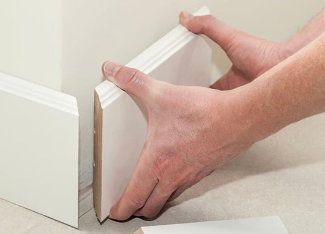 Une personne tient un morceau de moulure blanche dans ses mains.