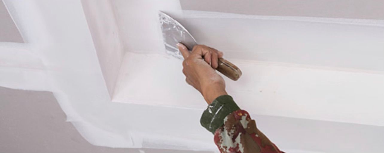 Une personne enduit un plafond avec une spatule.