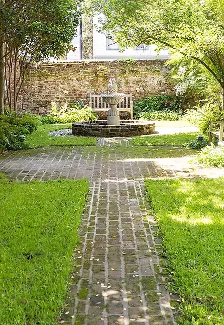 A brick walkway leading to a fountain in a garden.