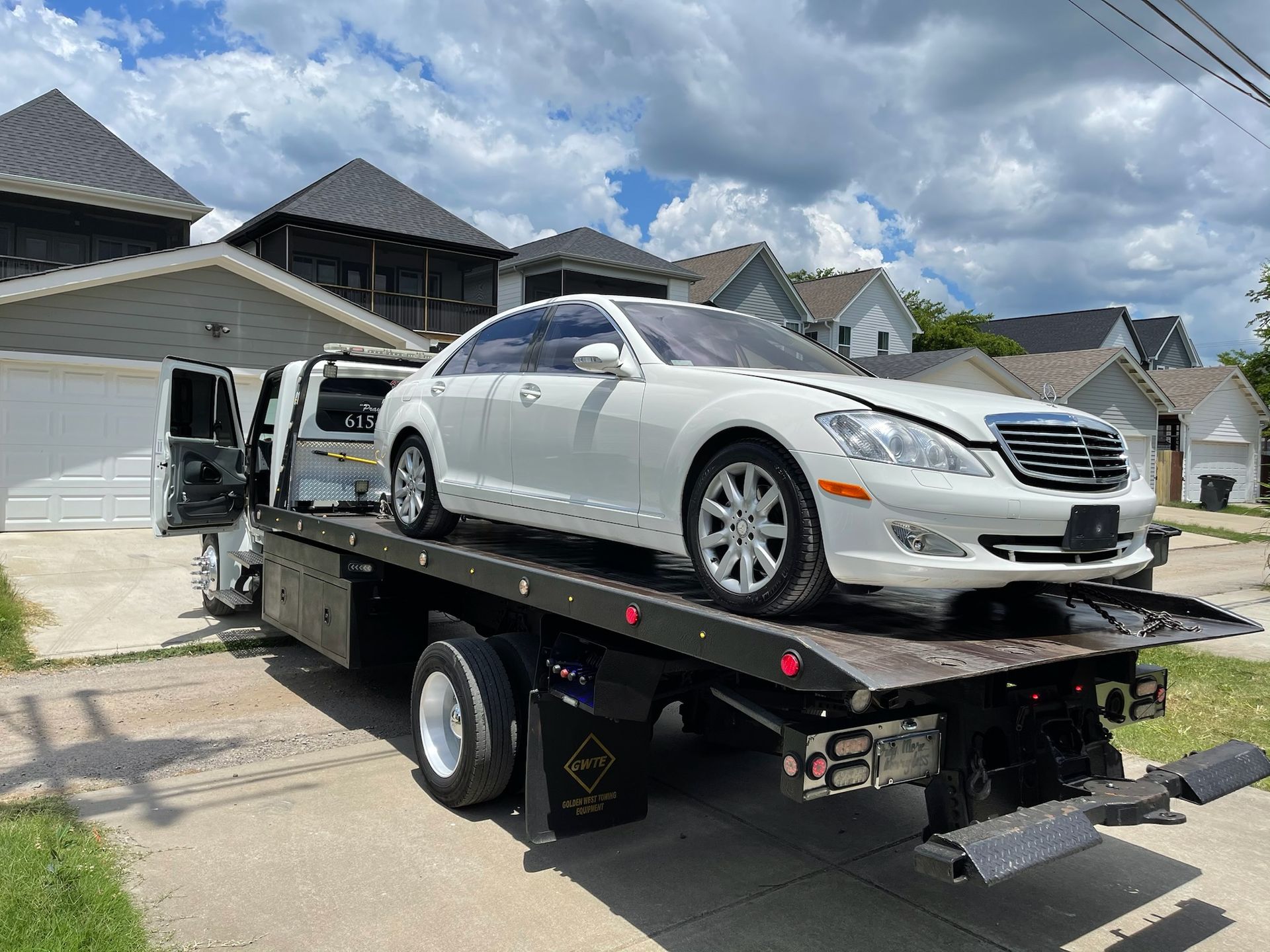 White Mercedes sedan loaded onto a black tow truck in a residential area.