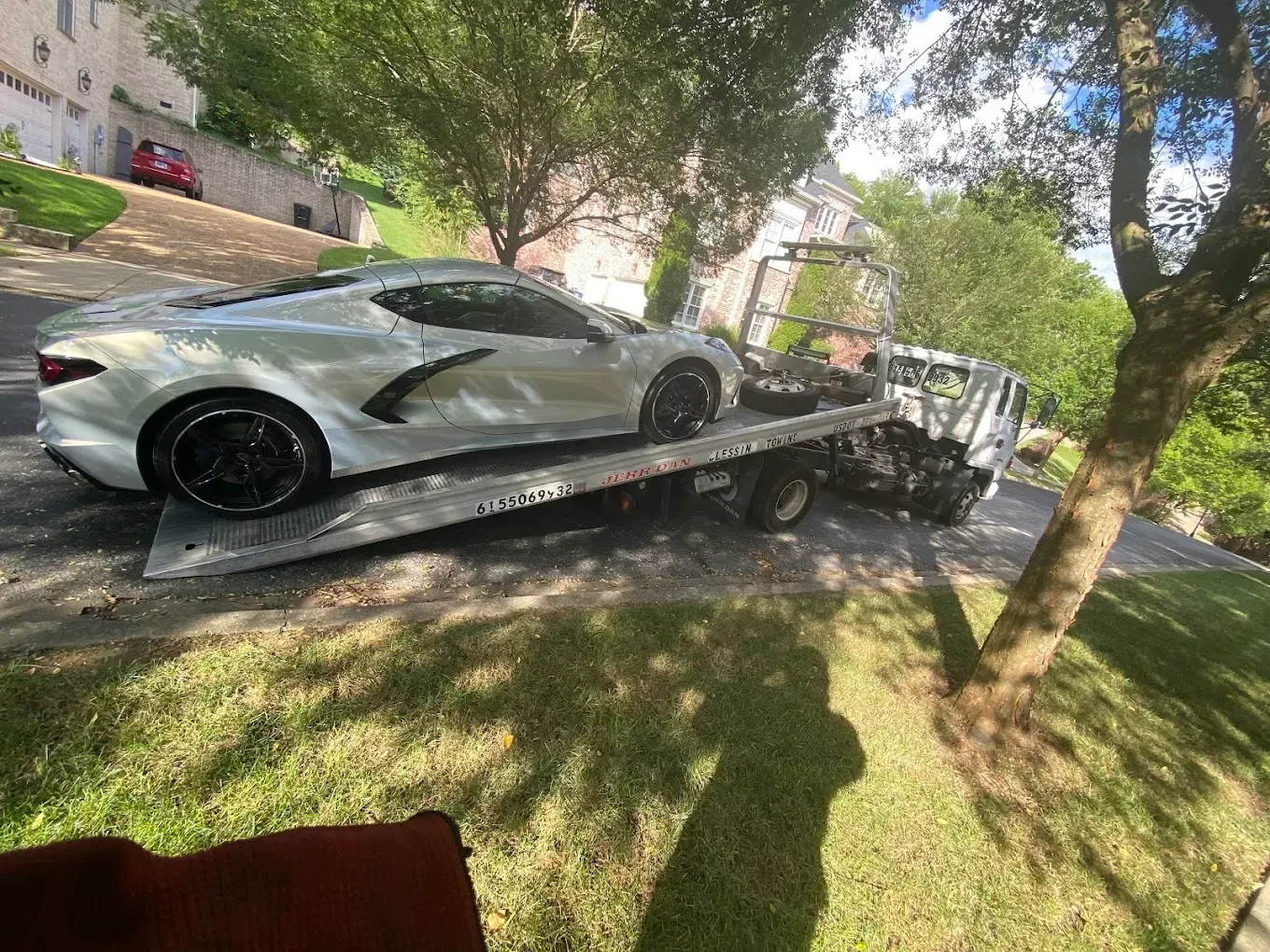 Silver sports car on a flatbed tow truck on a grassy hill.