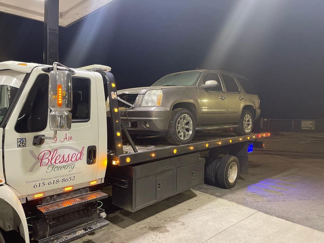 Tow truck with a gold SUV on its flatbed at night.