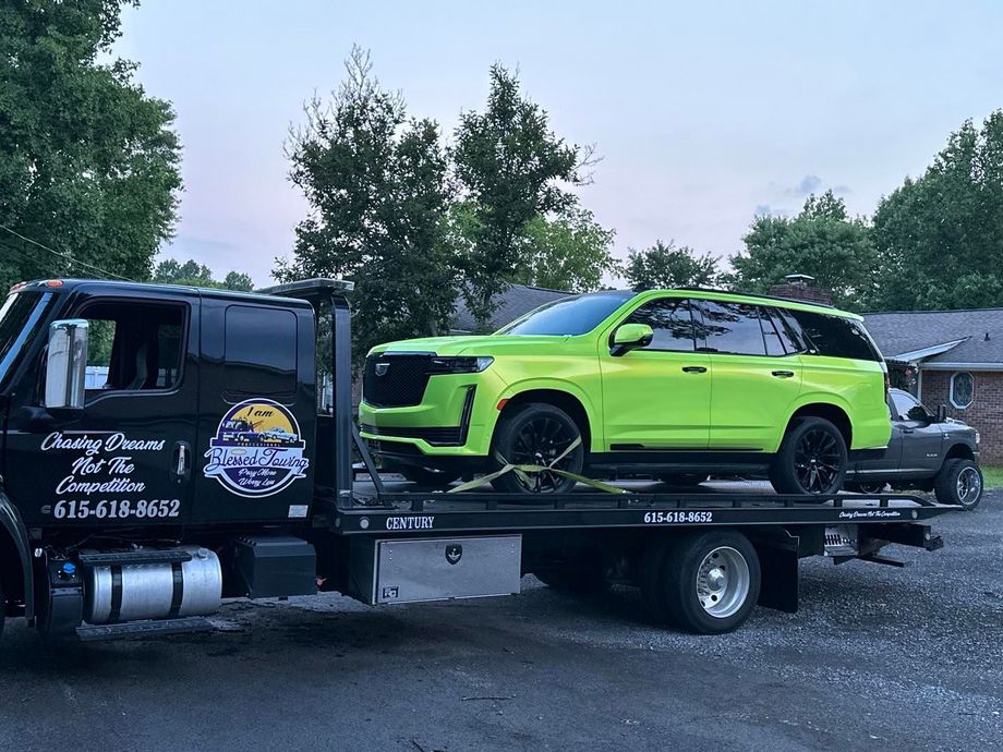 A lime green SUV is towed on a black tow truck in front of a house, cloudy sky in background.