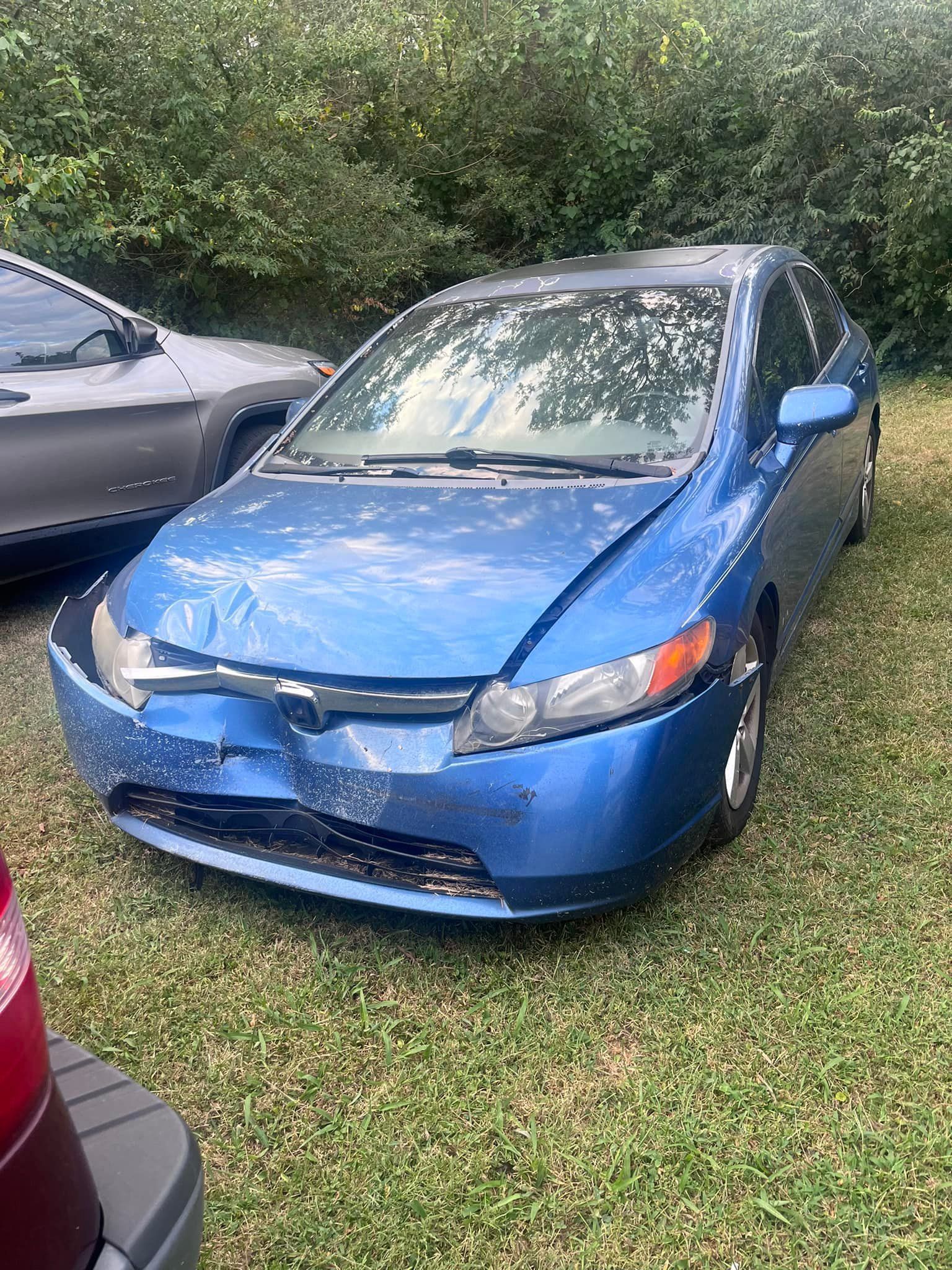 Blue Honda Civic with front-end damage parked on grass next to another car.
