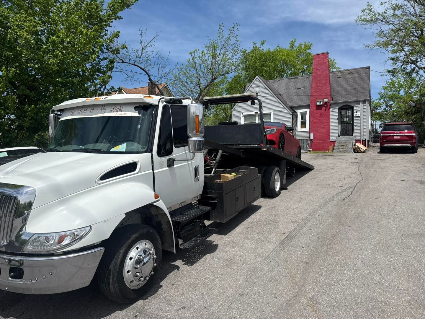 Tow truck in front of a house, red car on the flatbed, blue sky.