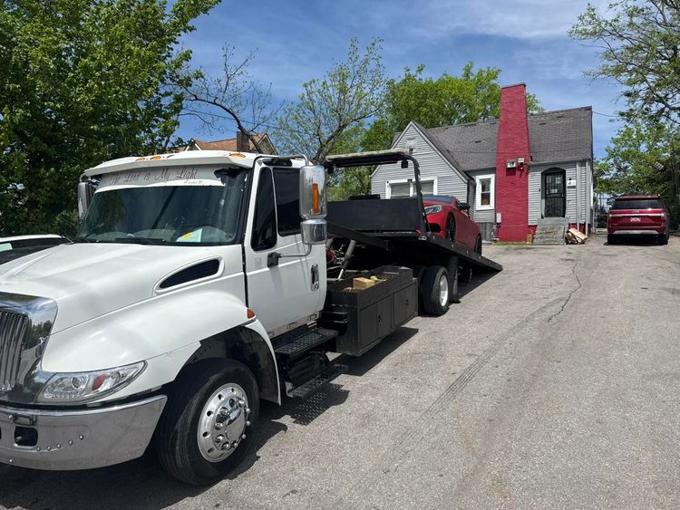 Tow truck in front of a house, red car on the flatbed, blue sky.