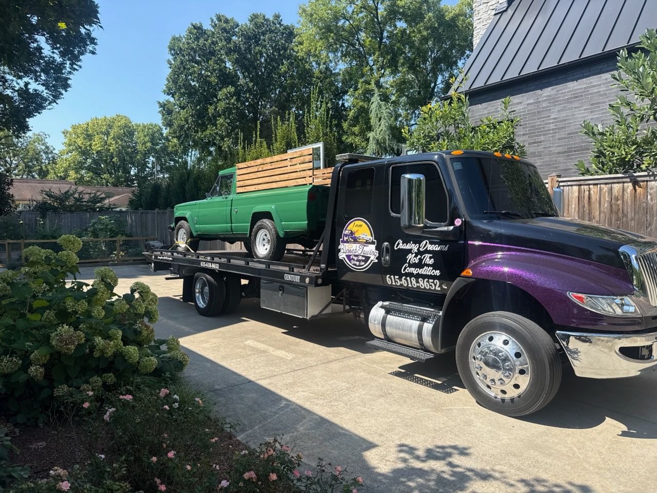 Green pickup truck on a black and purple tow truck, parked on a driveway.