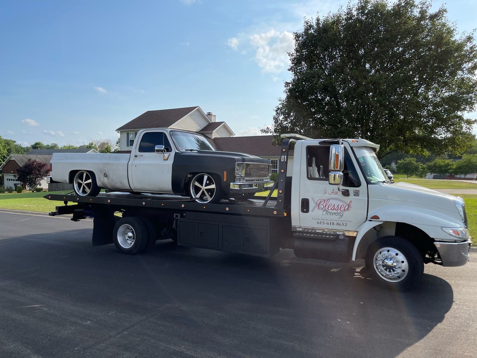 White tow truck carrying a two-tone, classic pickup truck on a sunny day.