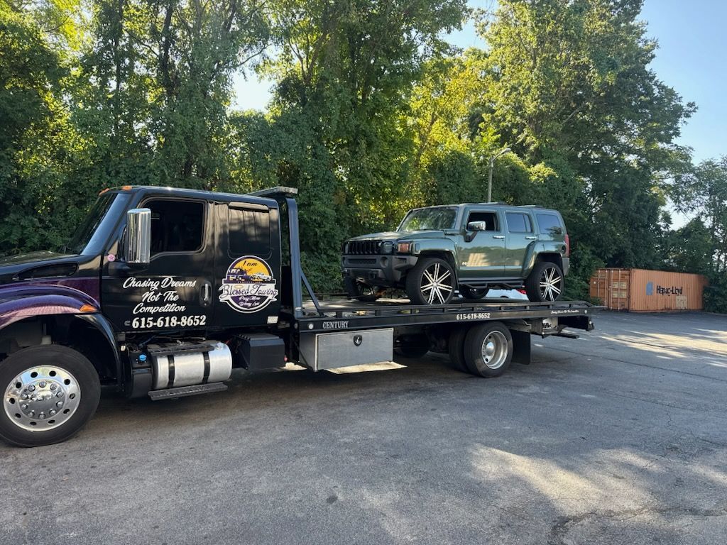 A black tow truck carries a green Hummer H3 in a parking lot.