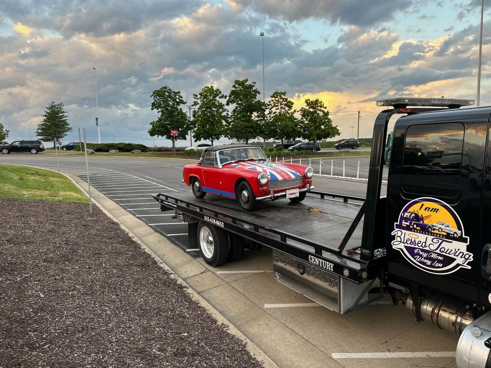 Red classic car on a flatbed tow truck. The car is on a road with trees and sky.