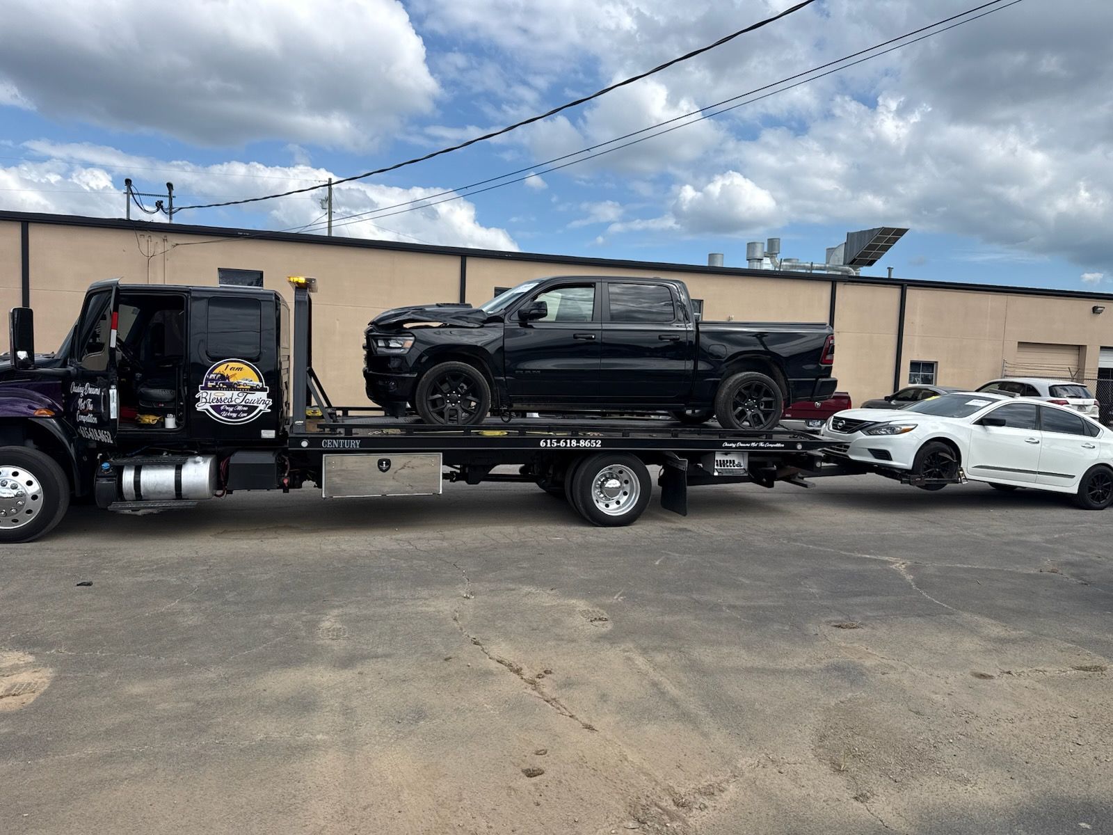 Tow truck carrying a black pickup truck and a white sedan on a sunny day.