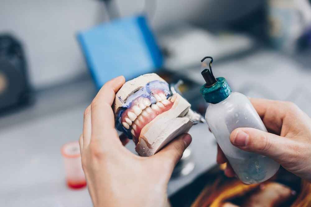 A Person Is Holding A Model Of Teeth And A Bottle Of Liquid — Port Denture Clinic In Port Macquarie, NSW