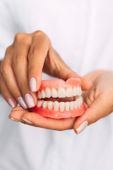 A Dentist Holding Dentures — Port Denture Clinic In Port Macquarie, NSW