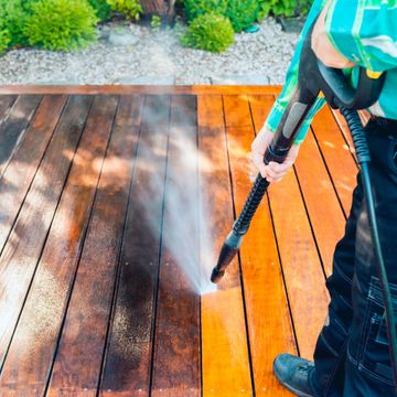 Nkomo Painting & Contracting | A man is cleaning a wooden deck with a high pressure washer.