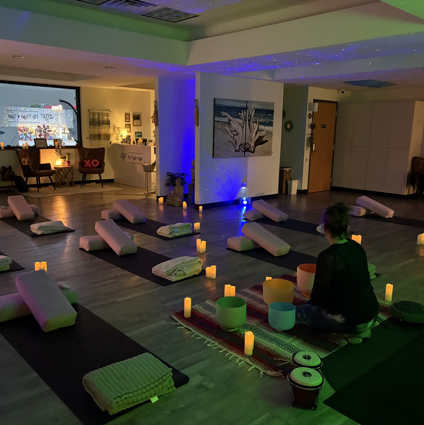 A man sits on a yoga mat in a room with candles and bowls