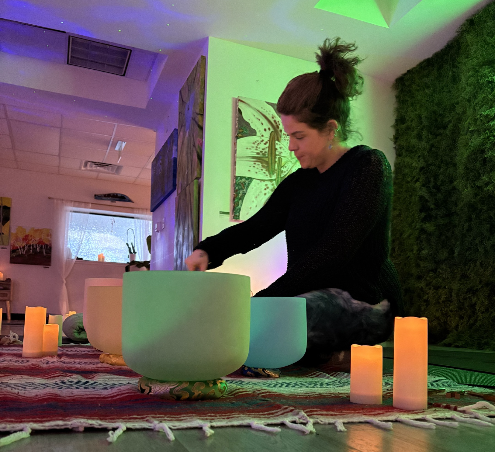 A woman is sitting on the floor playing a sound bowl surrounded by candles.