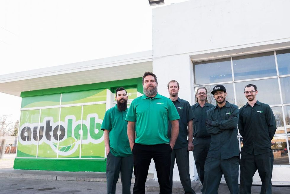 Group of six auto mechanics in green shirts stand outside an 