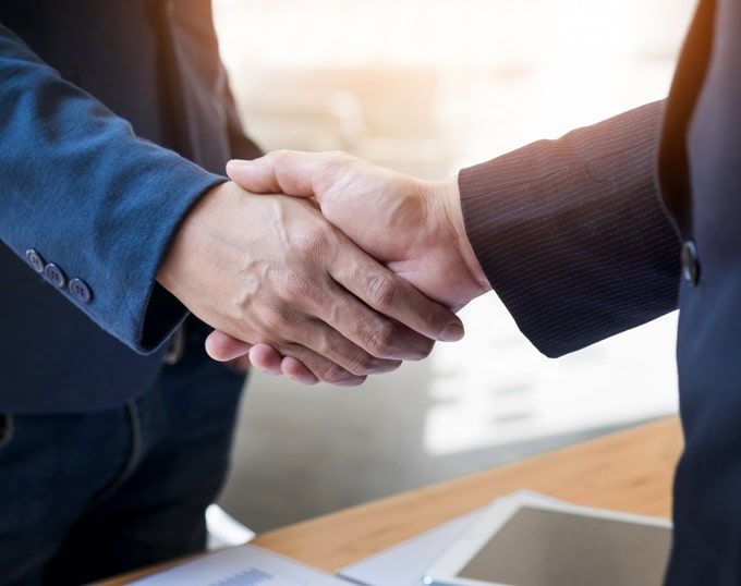 Dos hombres de traje se dan la mano sobre un escritorio, probablemente un acuerdo comercial.
