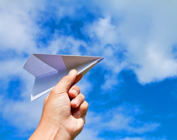 Mano sosteniendo un avión de papel contra un cielo azul brillante con nubes.