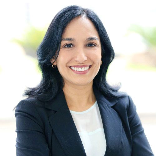 Mujer sonriente con cabello oscuro, vestida con un blazer y una camisa blanca.
