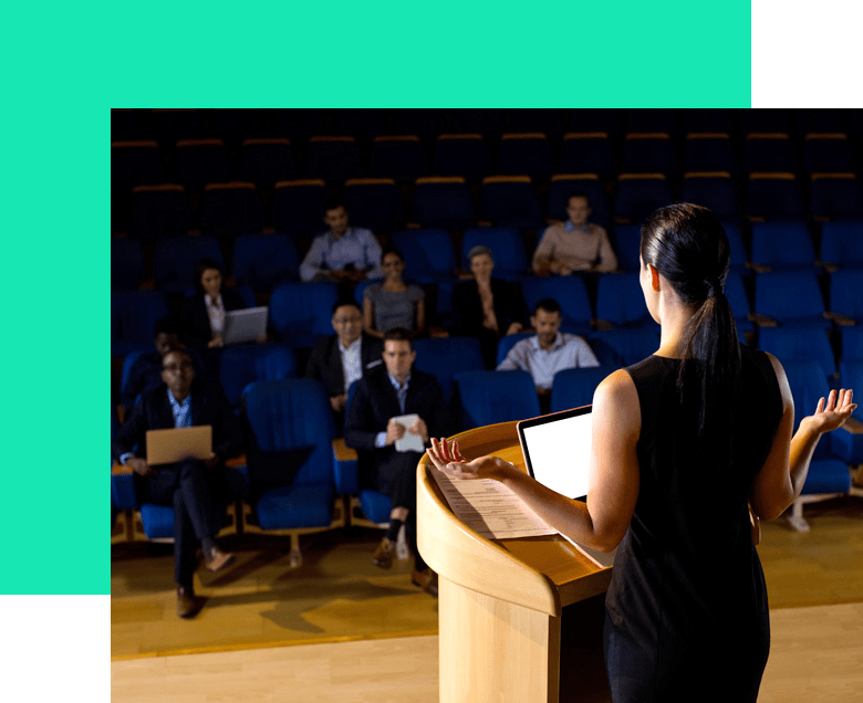Mujer dando una presentación en un podio en un auditorio oscuro ante una audiencia.