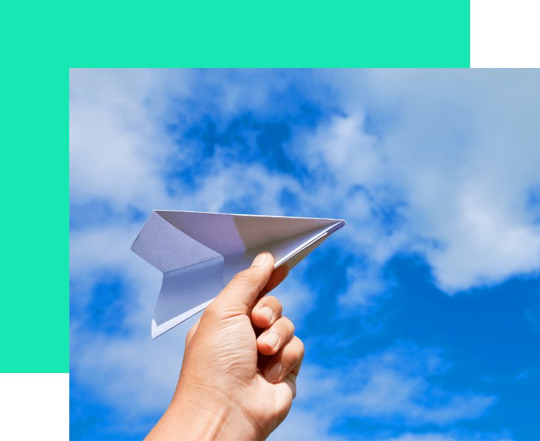 Mano sosteniendo un avión de papel, cielo azul con nubes en el fondo.