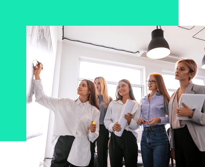 Un grupo de mujeres en una oficina haciendo una lluvia de ideas, una de ellas escribiendo en una pizarra.