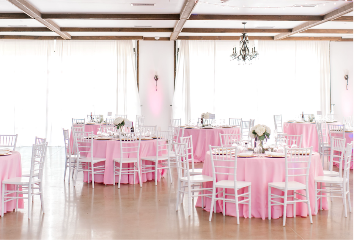 A large room with pink tables and chairs set up for a wedding reception.