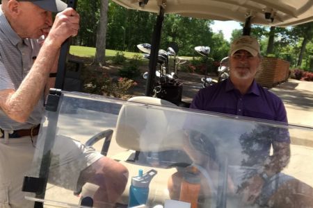 Two men are sitting in a golf cart talking to each other.
