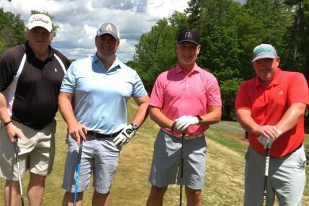 Four men are standing on a golf course holding golf clubs.