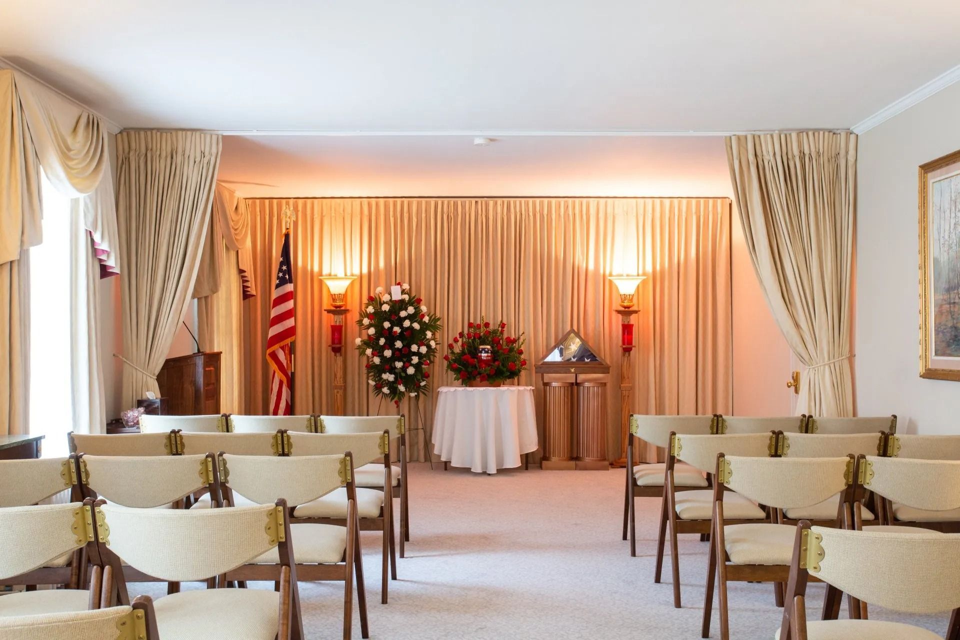 Memorial chapel with rows of chairs, casket, floral wreath, and soft draped lighting