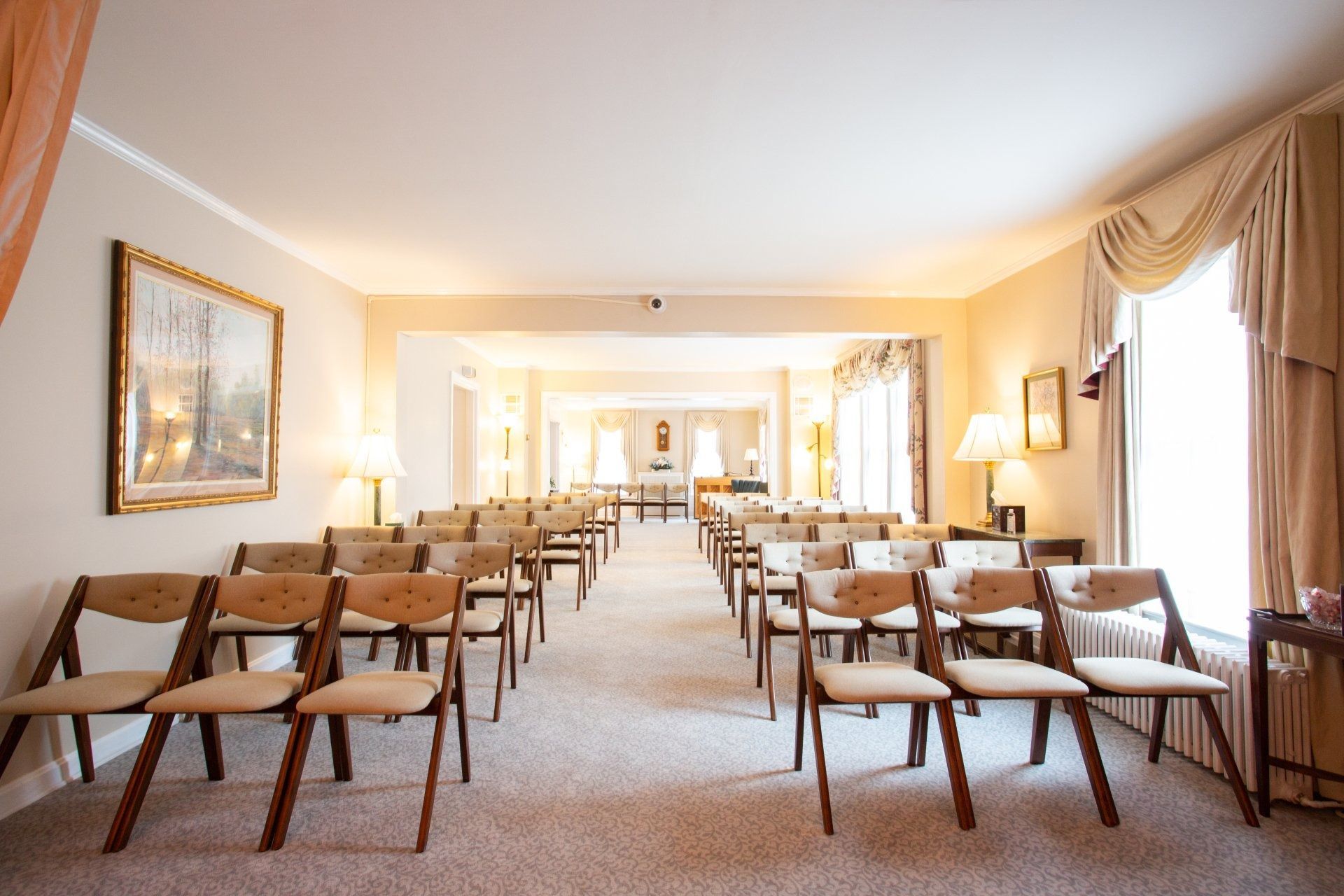 Empty elegant dining hall with rows of wooden chairs and tables, cream walls, and large curtained windows