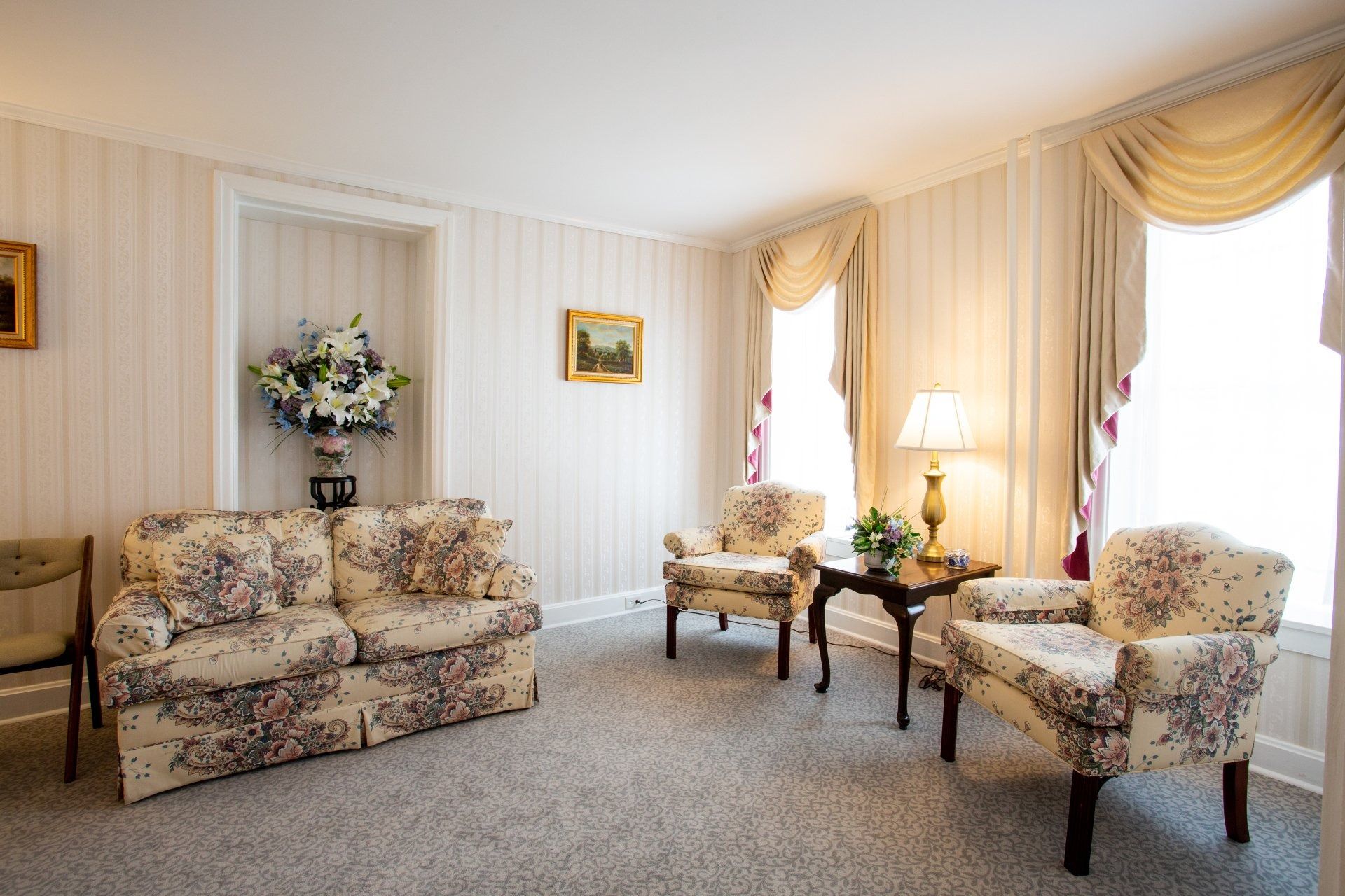 Elegant living room with floral sofas, armchairs, and tall windows with gold drapes