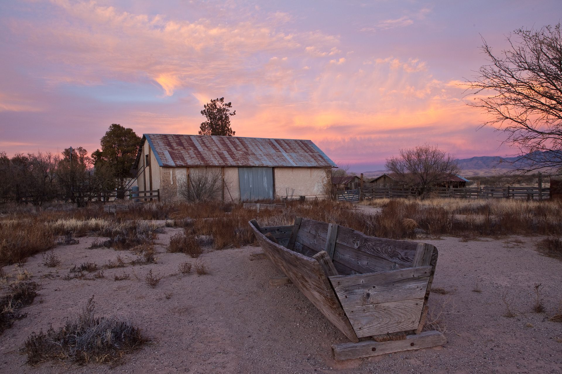 A boat is sitting in front of a barn at sunset.