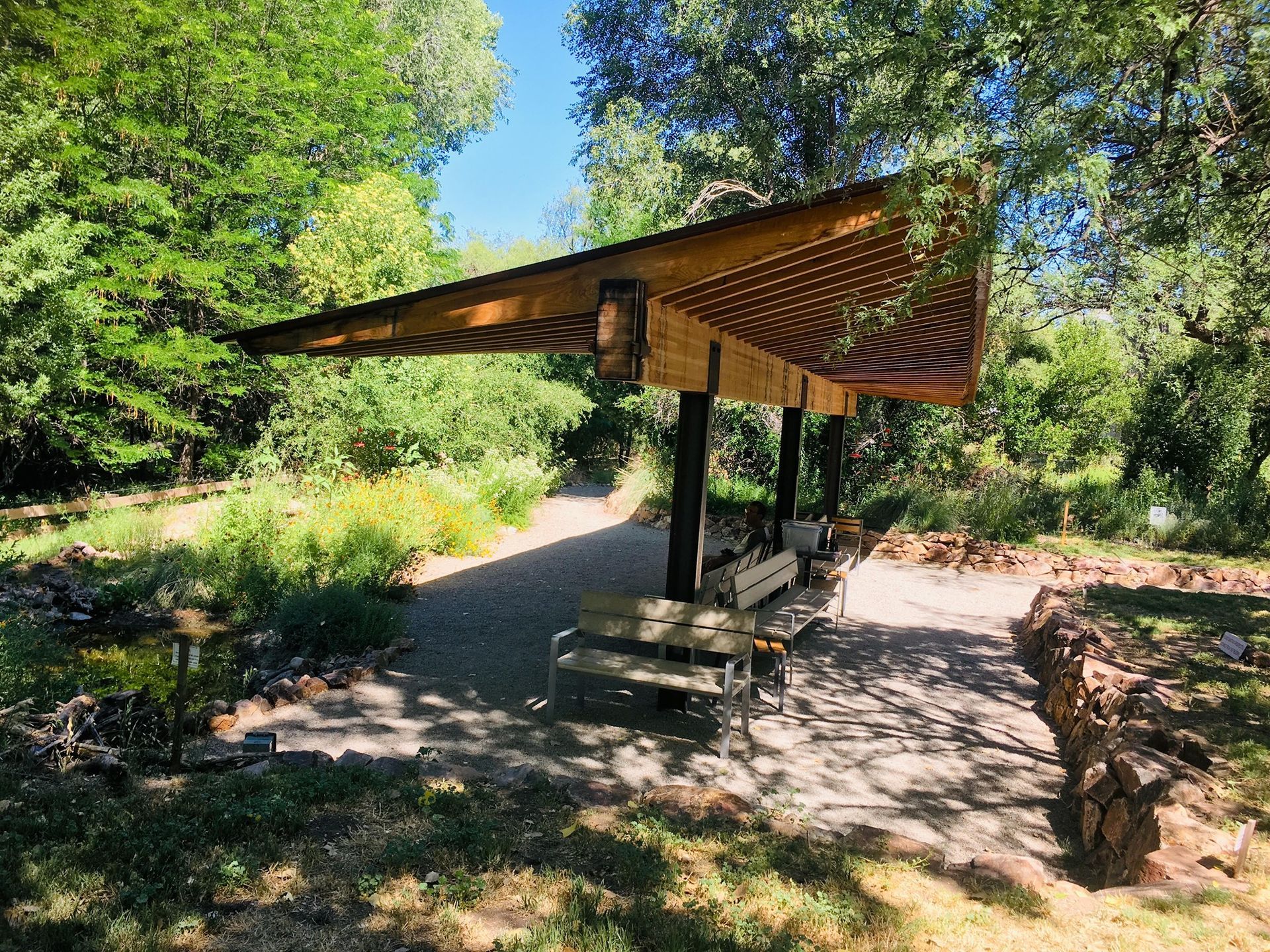 A wooden shelter with a bench underneath it in a park.