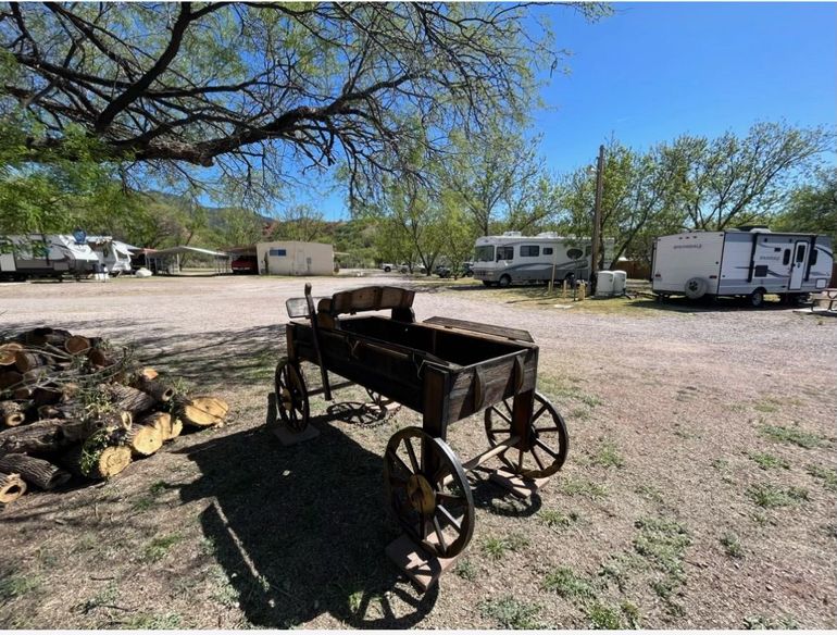 A wooden wagon is parked in a dirt lot next to a tree.