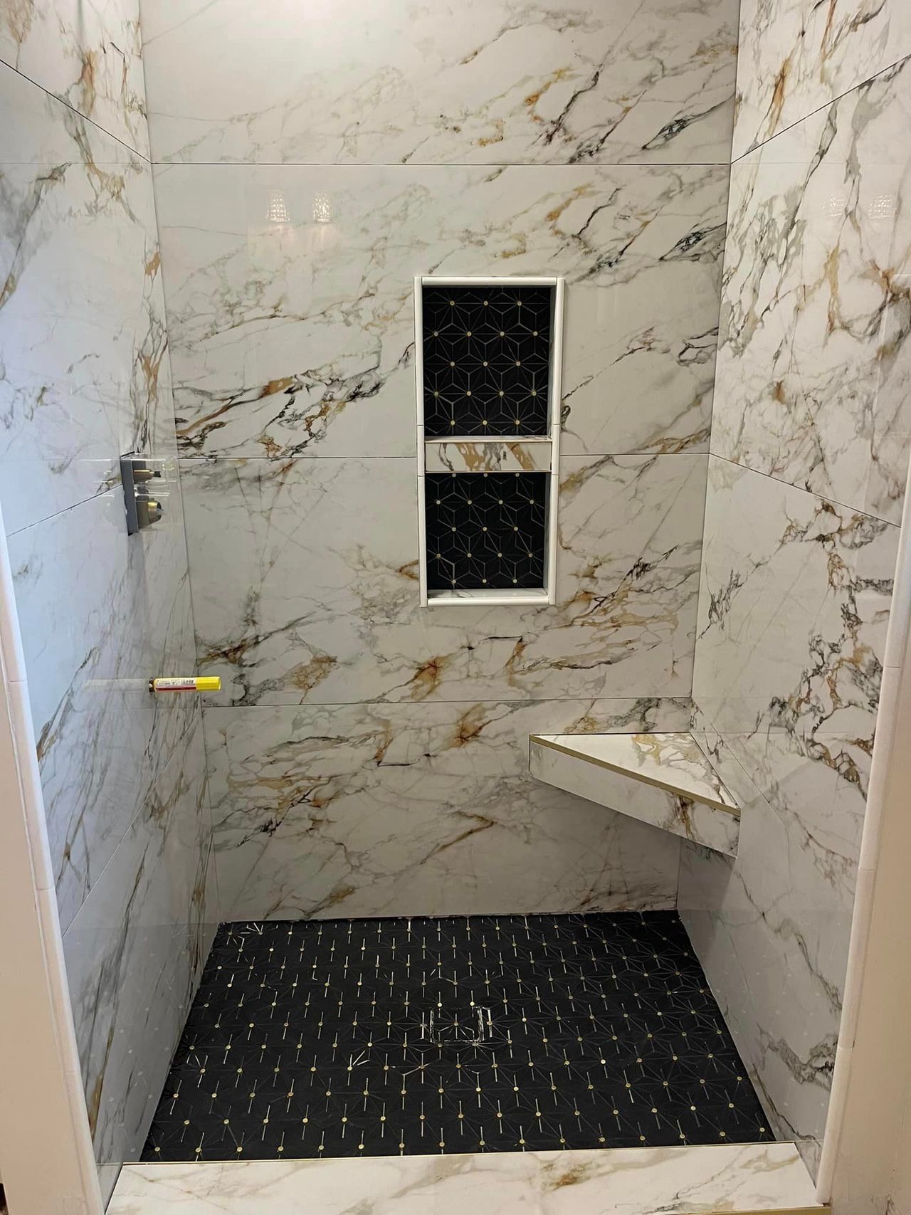 A shower with marble walls and a black tile floor.