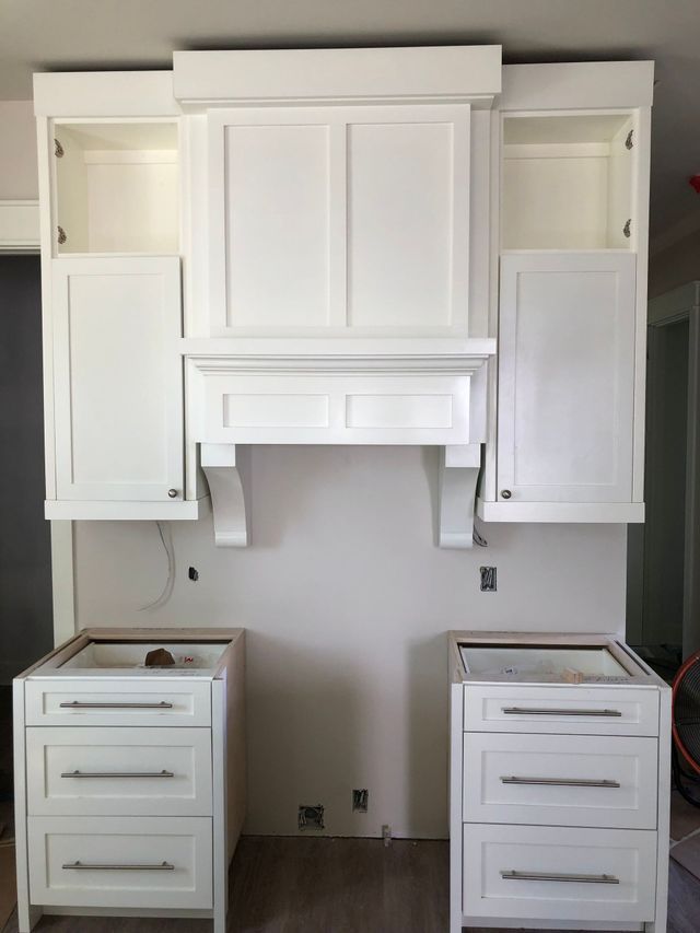 A kitchen with white cabinets , drawers and a hood.