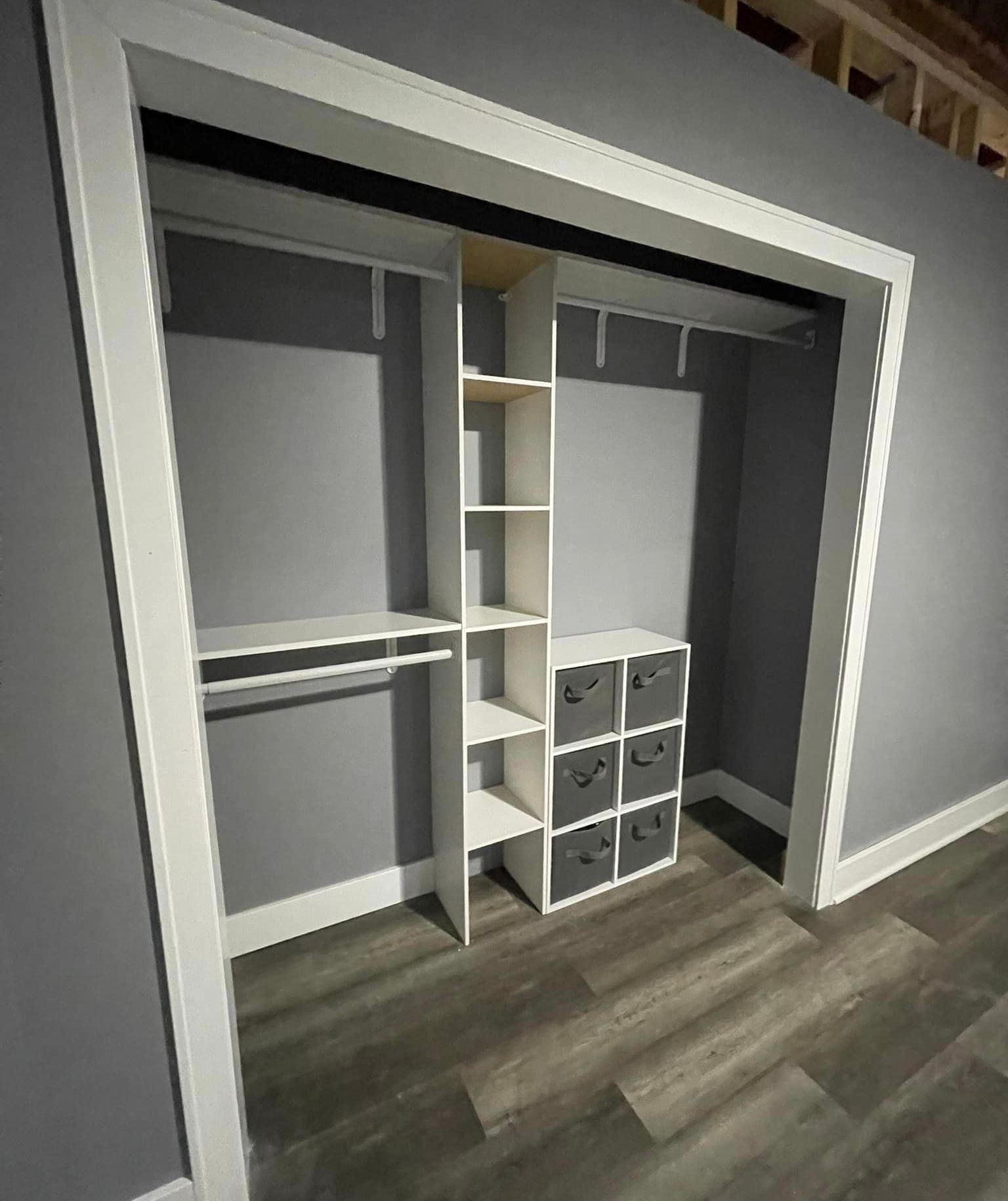 A walk in closet with gray walls and a wooden floor.