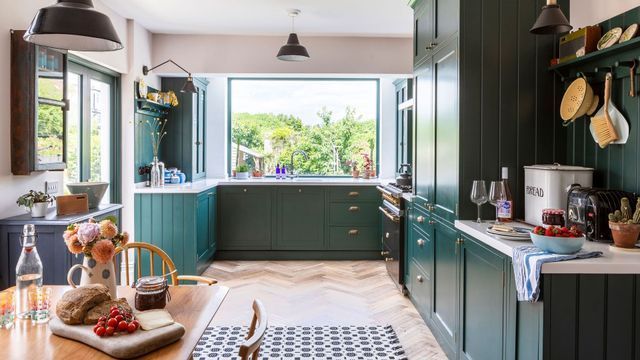 A kitchen with green cabinets , a table and a window.
