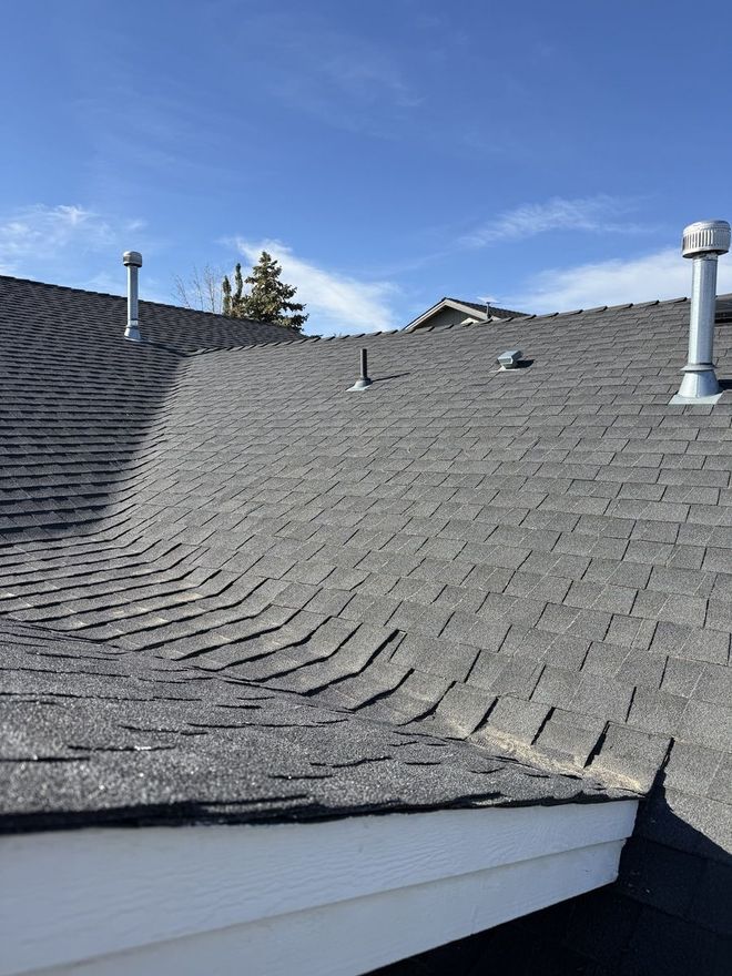 Man on a metal roof, possibly inspecting. House with brick and siding. Clear blue sky.