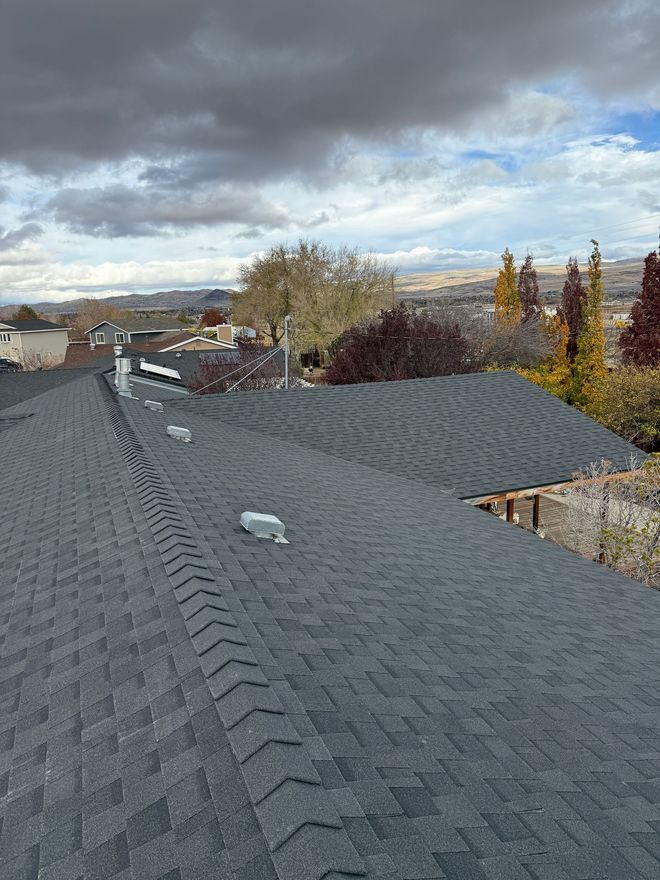 Aerial view of a brown shingled roof with dark patches, surrounded by green grass.