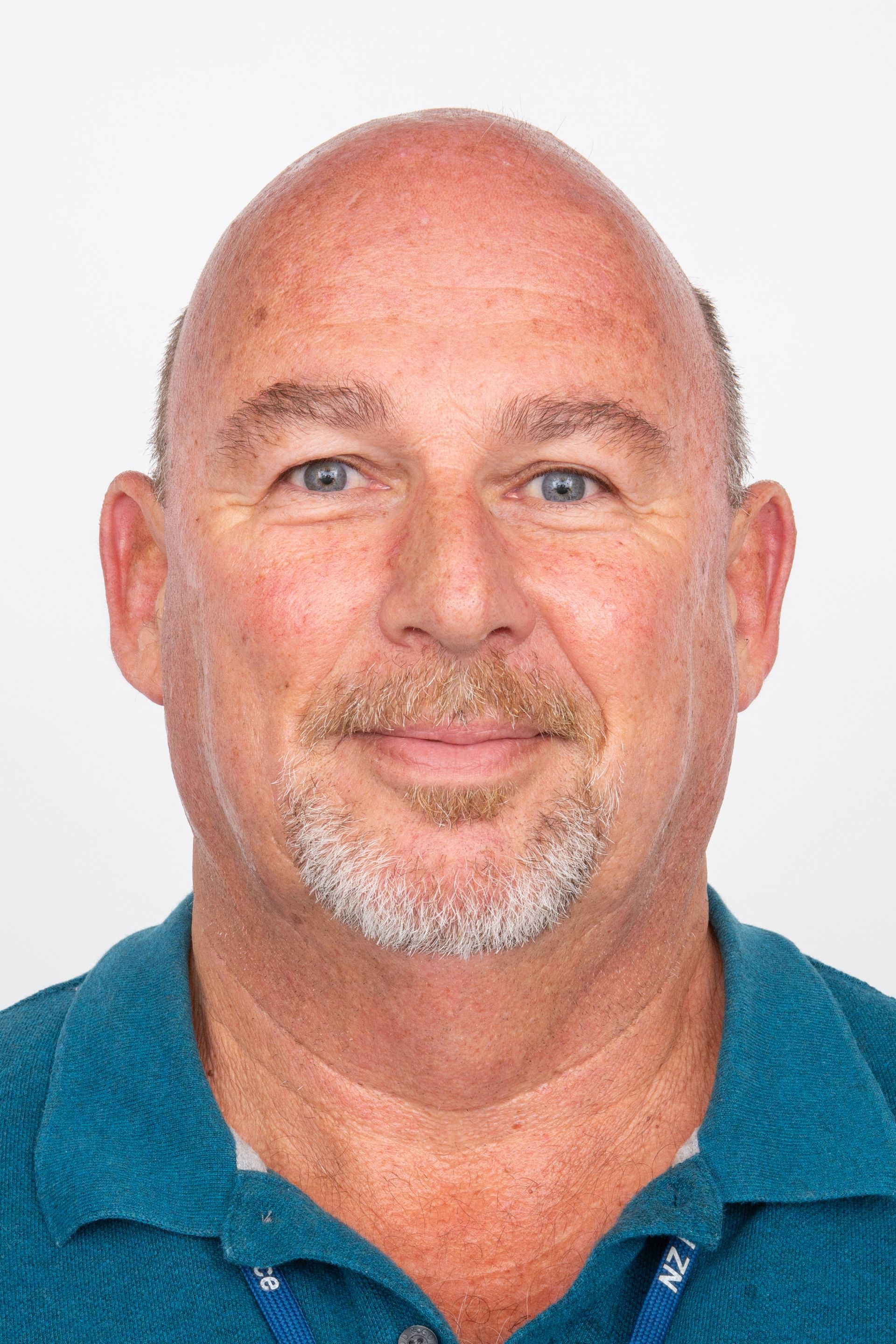 A bald man with a beard is wearing a blue shirt and smiling for the camera.