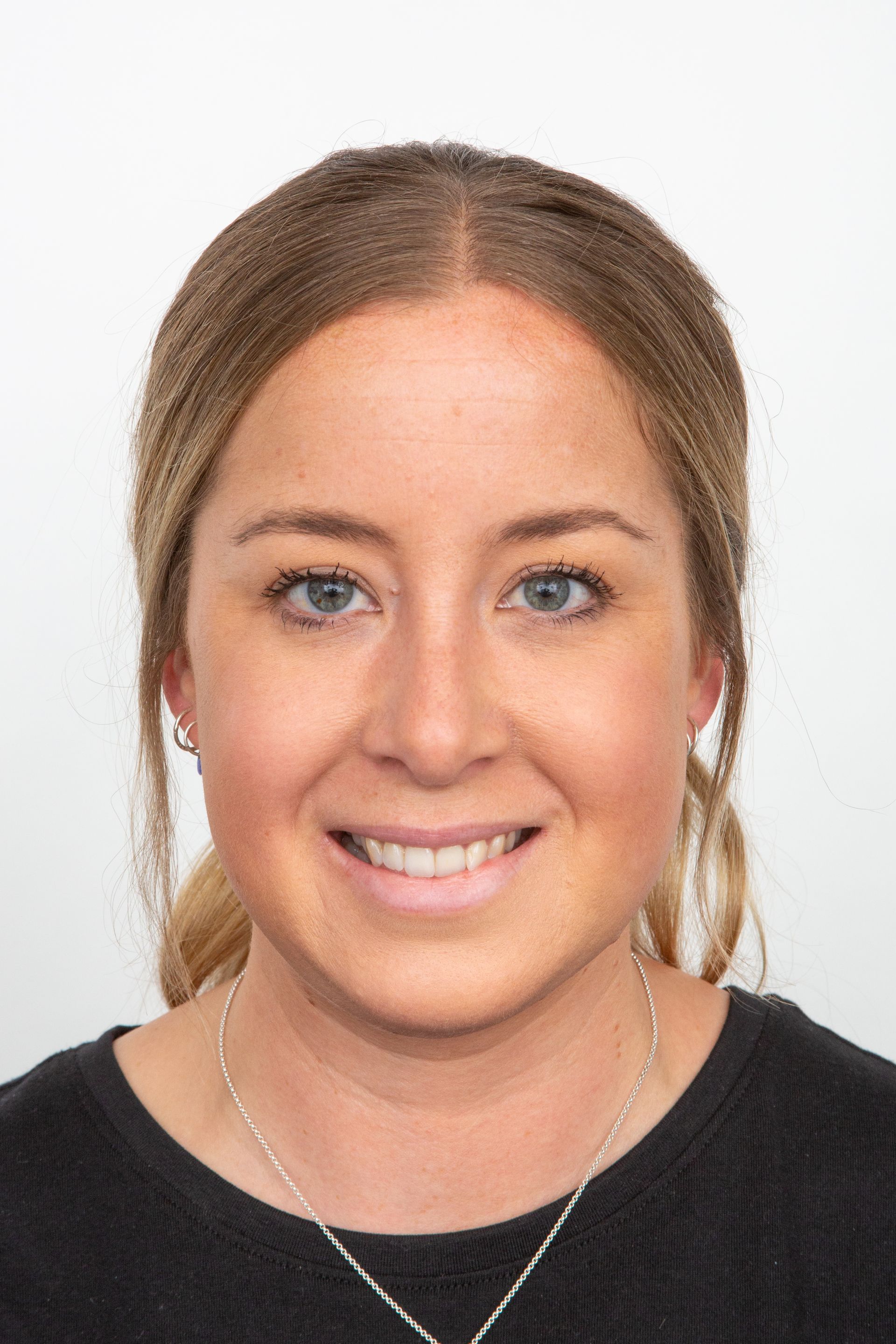 A woman wearing a black shirt and a necklace is smiling for the camera.
