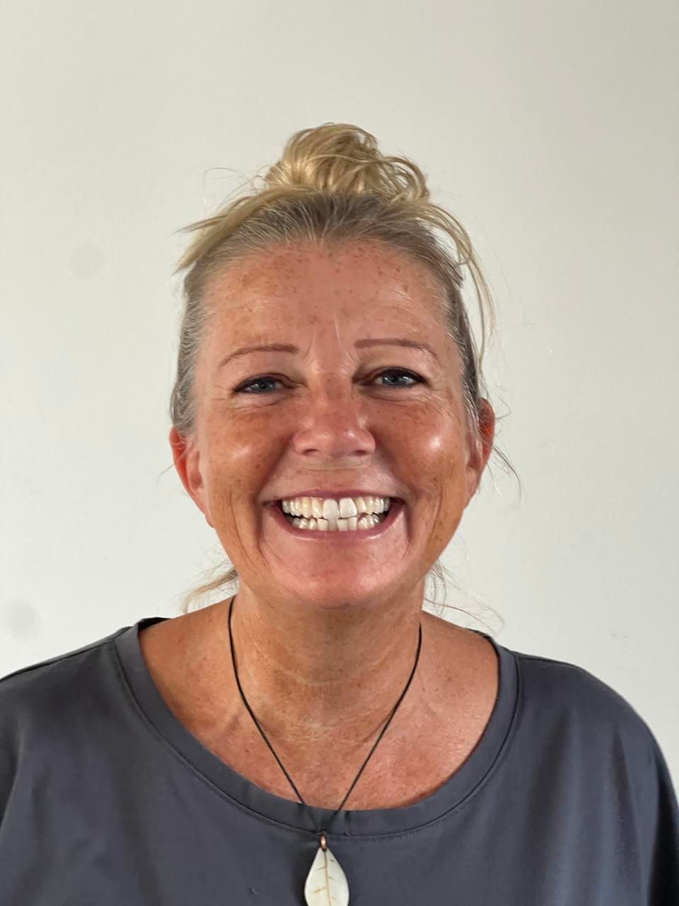 A woman wearing a necklace and a bun is smiling for the camera.