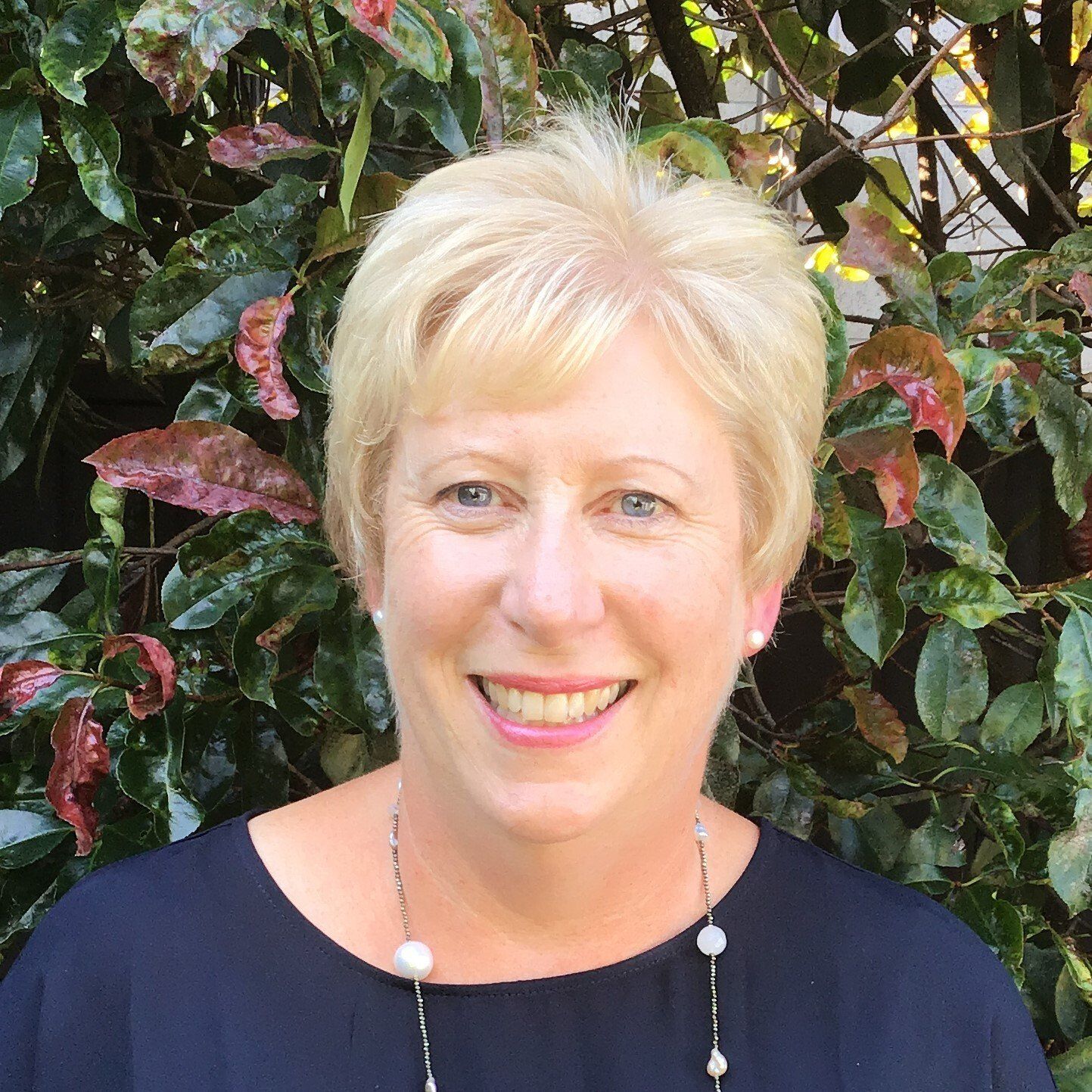A woman is smiling for the camera in front of a bush.